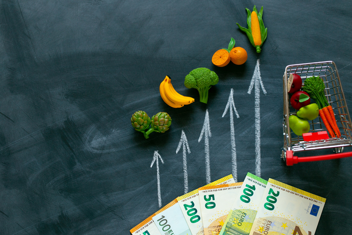 Rising food prices in the European Union.Grocery basket in Europe.Decorative supermarket trolley with groceries and up arrows on black chalk board background..Vegetables and fruits price increase.